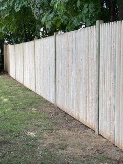 Tall white wooden fence along a grassy yard with trees overhead