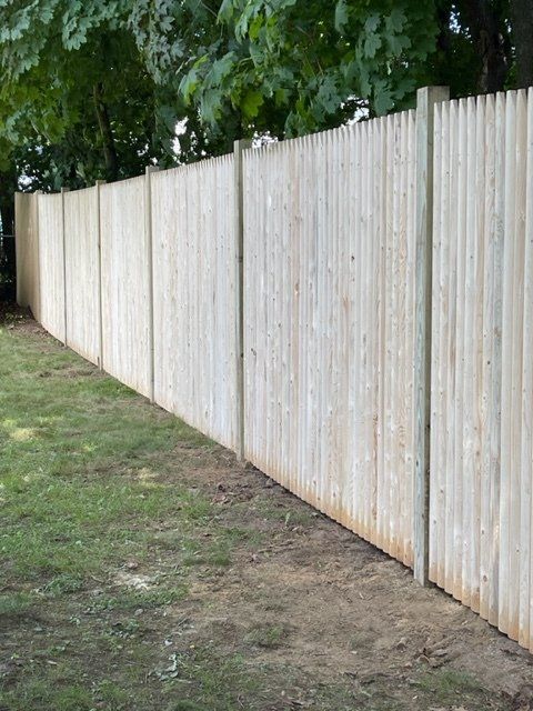 Tall white wooden fence along a grassy dirt path under trees