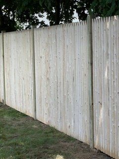 Tall weathered white wooden fence beside a grassy yard and trees