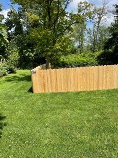 Wooden fence in a sunny grassy yard with trees in the background.