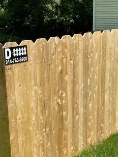 Wooden fence with a black-and-white sign labeled “D” and a phone number in a backyard.