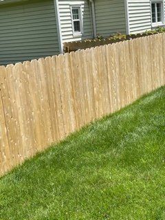 Wooden backyard fence beside a green lawn, with a house in the background.
