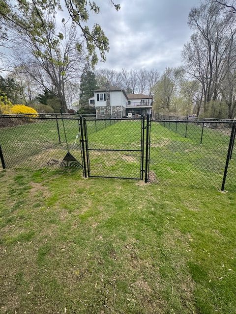 Chain-link gate in a grassy backyard, with a white house and trees in the background.