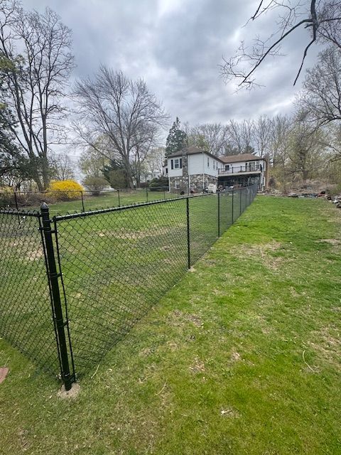Black chain-link fence in a grassy yard with leafless trees and a house in the background