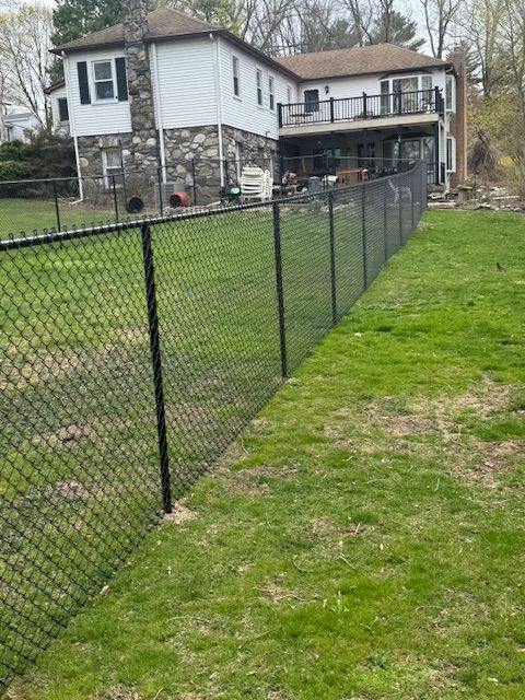 Chain-link fence along a grassy yard beside a white house with a deck and stone foundation.