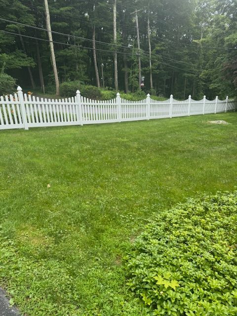 White picket fence bordering a green lawn and wooded yard