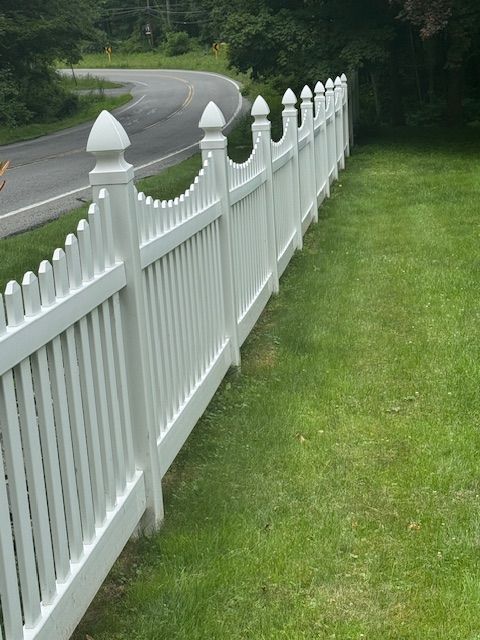 White picket fence along a curved road beside a grassy lawn and trees