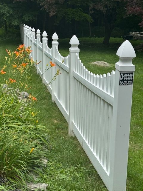 White picket fence beside orange flowers in a green garden.