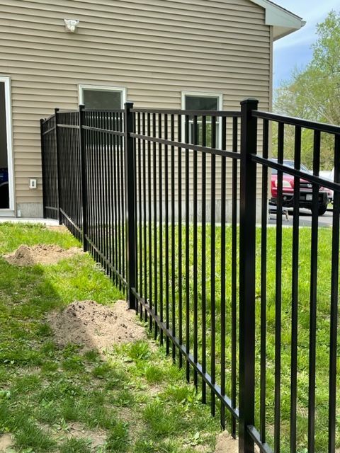 Black metal fence along a grassy side yard beside a beige house, with a driveway and red car in back.