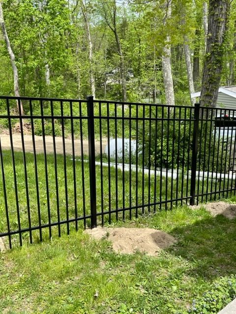 Black metal fence in a grassy yard beside a wooded path and small stream.