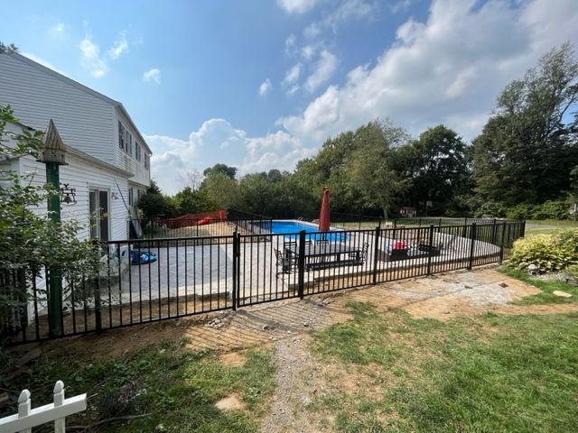Backyard pool behind black fence beside a white house on a sunny day