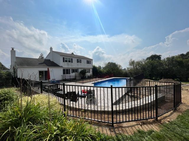 Backyard with a fenced-in swimming pool beside a white house under a bright blue sky
