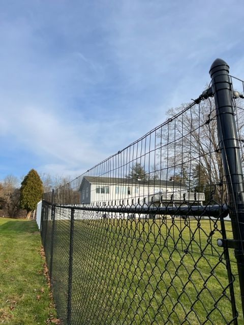 Chain-link fence and tall black post along a grassy field under a blue sky.