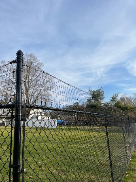Chain-link fence beside a grassy field under a cloudy blue sky