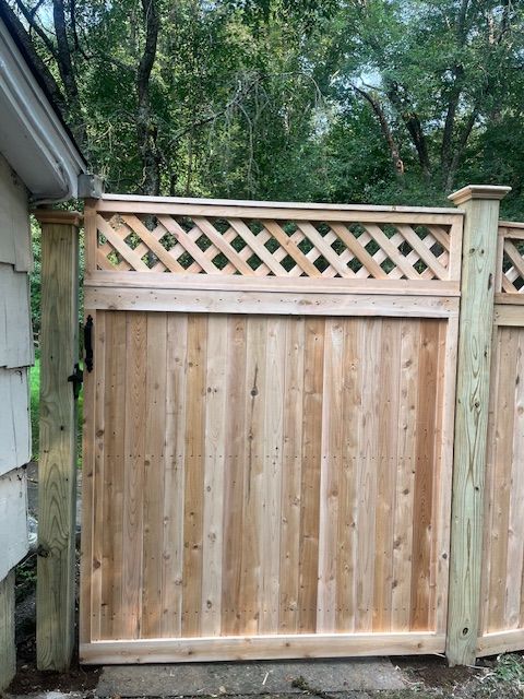 Wooden backyard privacy gate with lattice top beside a house and trees