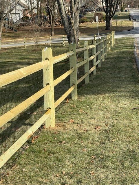 Yellow wooden fence beside a grassy path in a park, with trees and a pond in the background