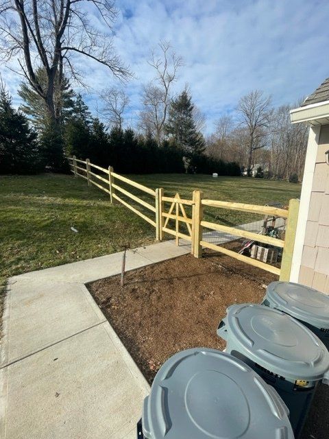 Backyard concrete path and wooden ramp with railing beside trash bins, leading to a grassy yard.