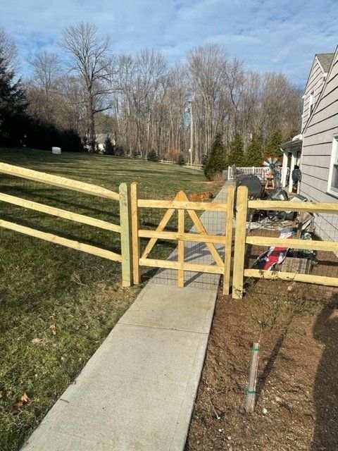 Wooden gate blocking a concrete walkway beside a house and grassy backyard.