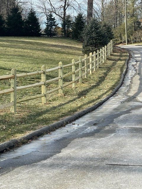 Curving paved road beside a wooden fence and grassy hillside on a sunny day