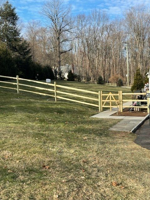 Wooden fence and gate beside a grassy yard with leafless trees in the background