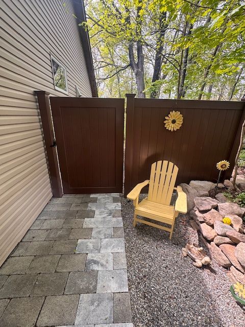 Narrow stone path beside house leads to brown gate and wooden chair in a small fenced patio garden