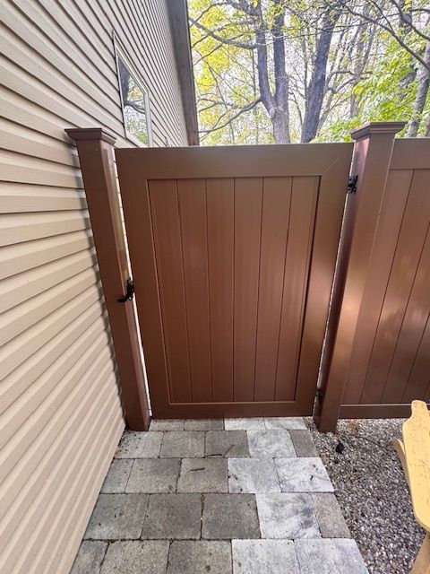 Wooden gate beside a house, leading from a paver walkway to a gravel yard.