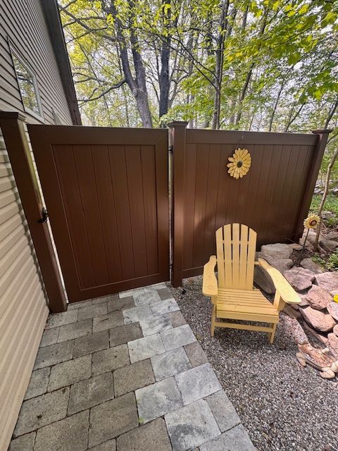 Small stone patio with brown privacy gates, a yellow wooden chair, and a decorative sun on the wall.