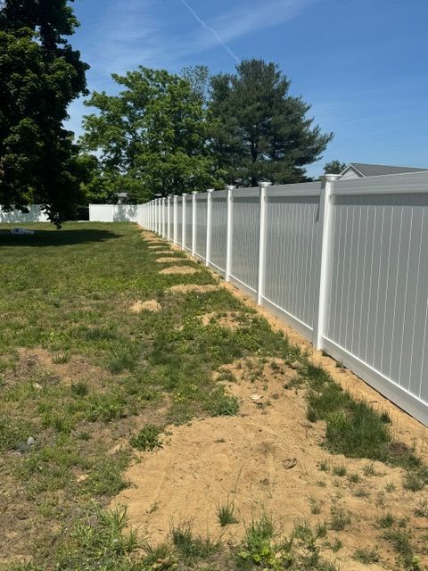 White vinyl fence along a grassy dirt yard under a sunny blue sky