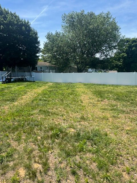 Grassy backyard with a white fence, large tree, and blue sky on a sunny day