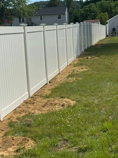 Long white vinyl fence along a grassy backyard with patchy dirt near the base