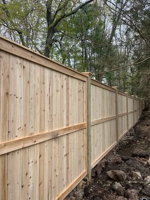 Wooden privacy fence along a wooded yard with rocks beside it