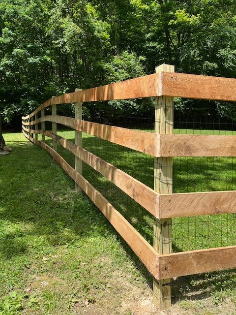 Wooden split-rail fence along a grassy path beside dense green trees