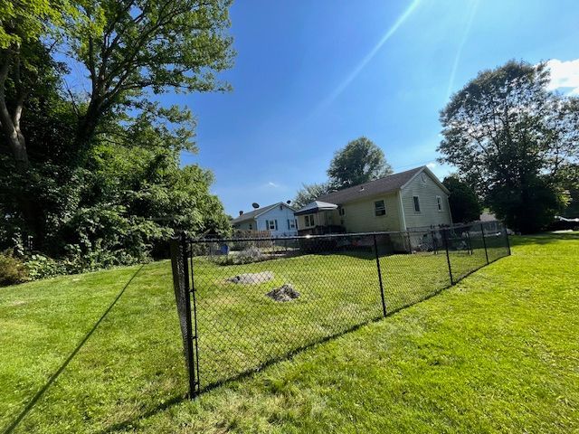Backyard with chain-link fence, green lawn, and a beige house under a bright blue sky