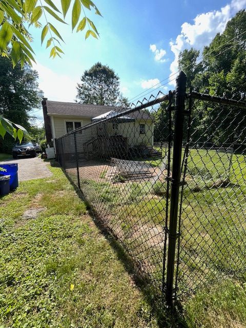 Backyard with chain-link fence, grassy yard, small patio, and a house under a sunny blue sky