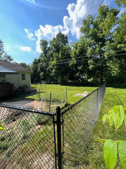 Chain-link fence around a grassy backyard beside a house under a bright blue sky with clouds.