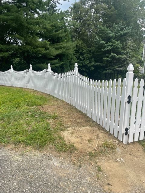 White picket fence curving along a grassy yard with trees in the background