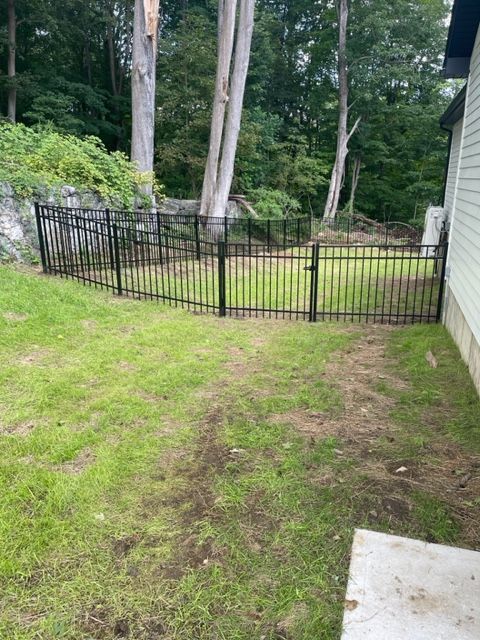 Small fenced backyard with grass, trees, and a concrete patio beside a house