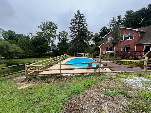 Backyard with covered pool, wooden fence, and red brick house surrounded by trees