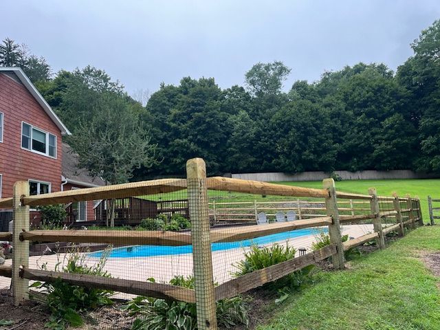 Backyard pool with wooden fence beside a red brick house and grassy yard