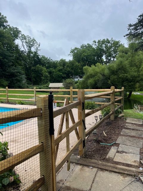 Wooden gate beside a backyard pool with stone path and green trees in the background