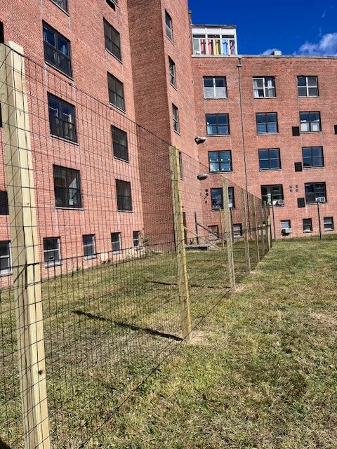 Brick apartment buildings beside a fenced grassy courtyard on a sunny day