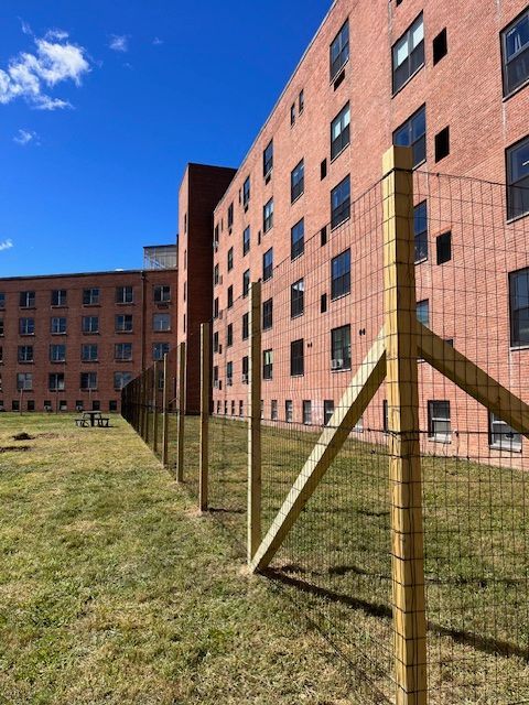 Long brick apartment buildings behind a wire fence on a grassy lawn under a blue sky