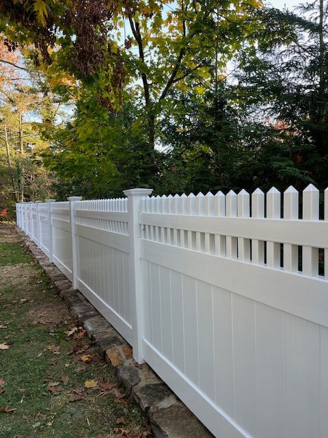 White vinyl picket fence along a wooded yard in autumn