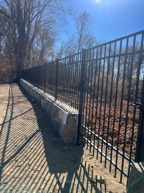 Black metal fence along a sunlit sidewalk beside leafless trees and fallen autumn leaves.