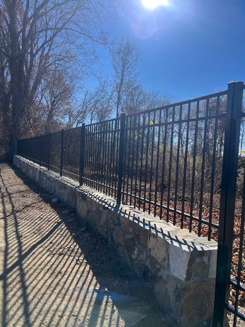 Stone retaining wall and black metal fence along a sunlit path with leafless trees and long shadows