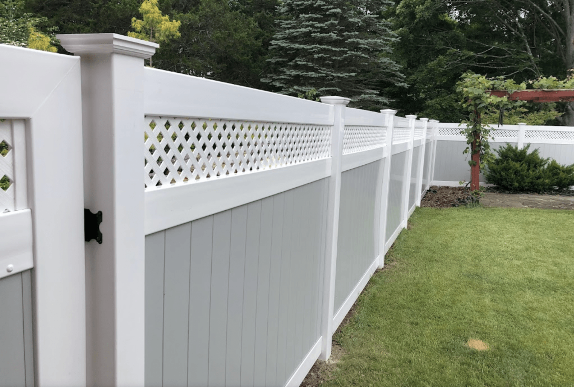 White vinyl privacy fence with lattice top bordering a green lawn