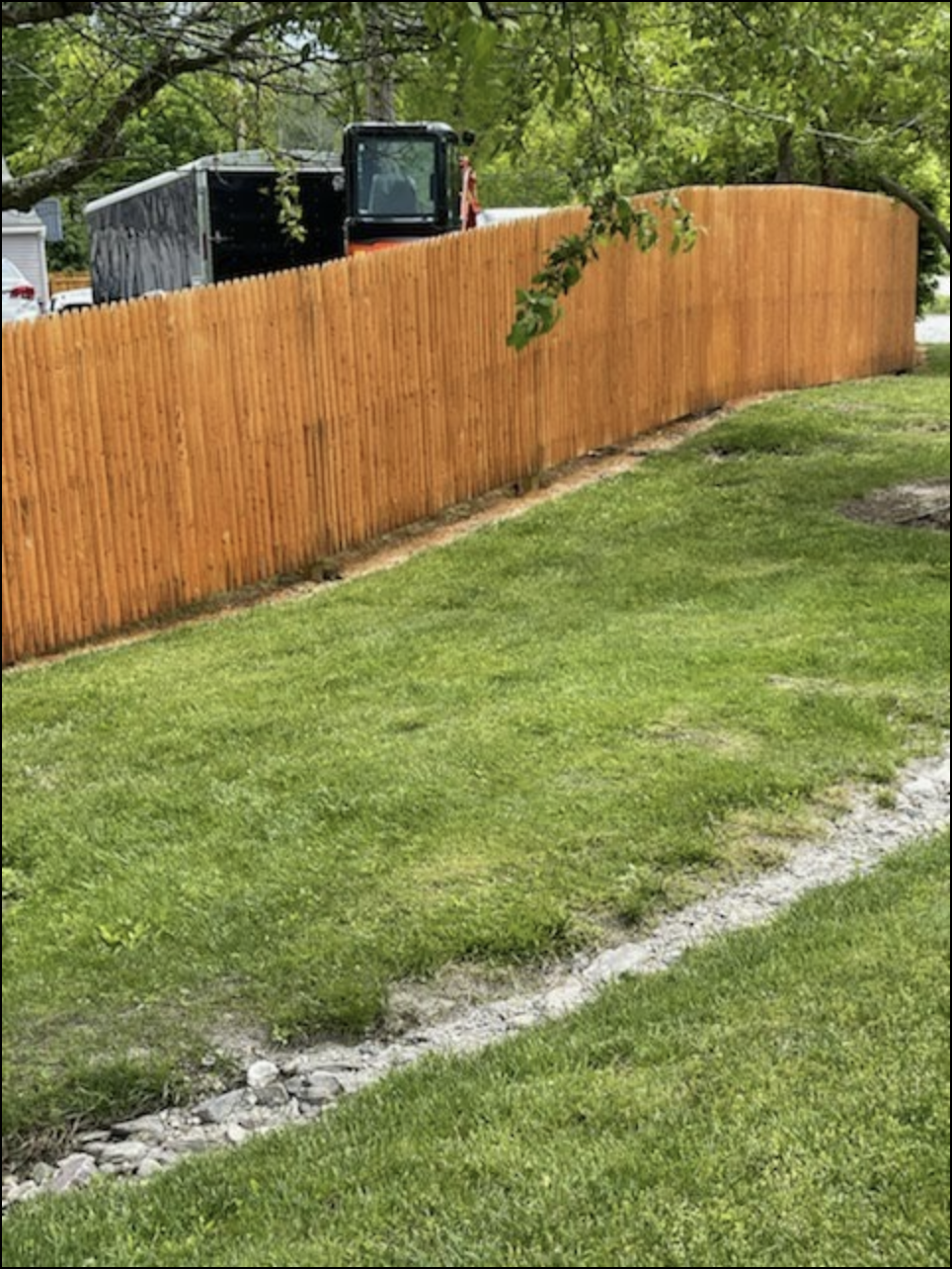 Orange wooden fence beside a grassy yard with a backhoe behind it