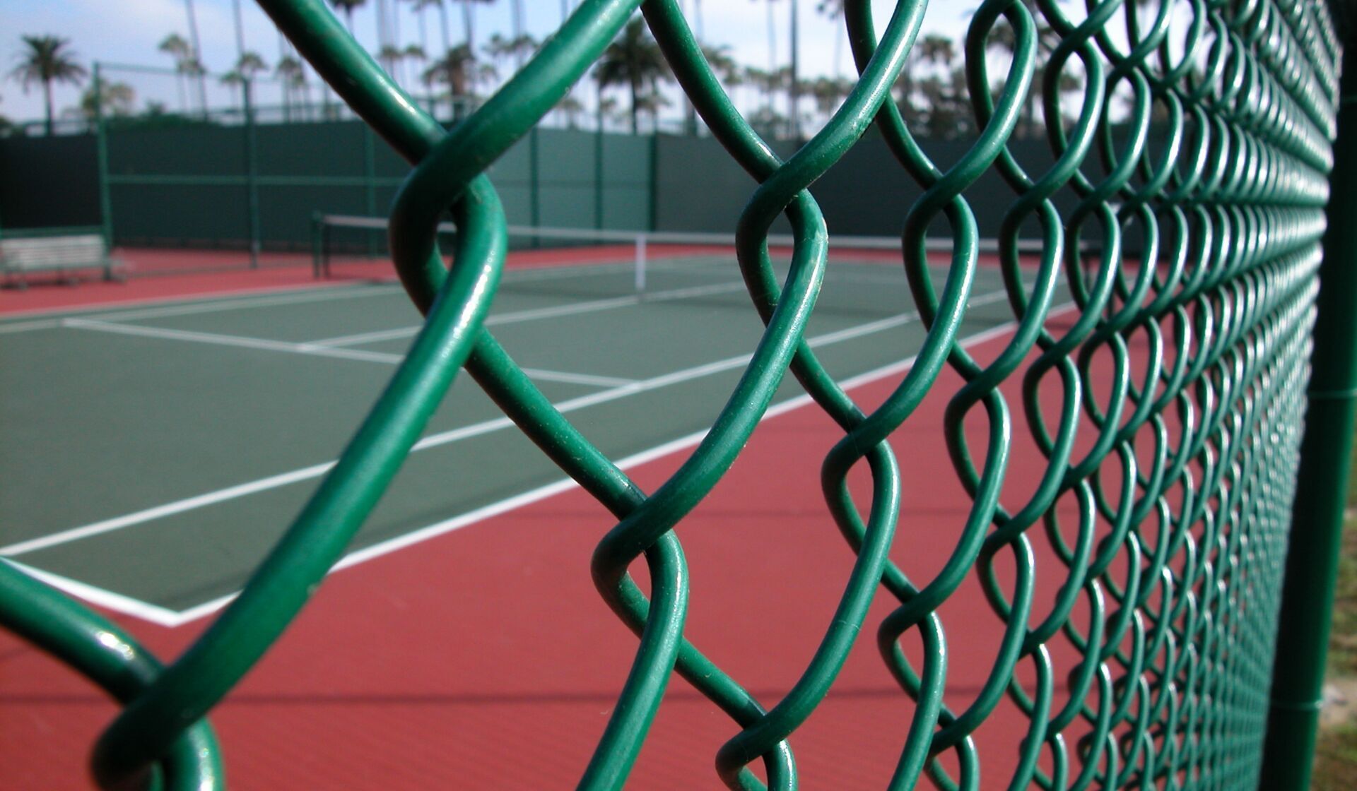 Green chain-link fence beside a red and green tennis court