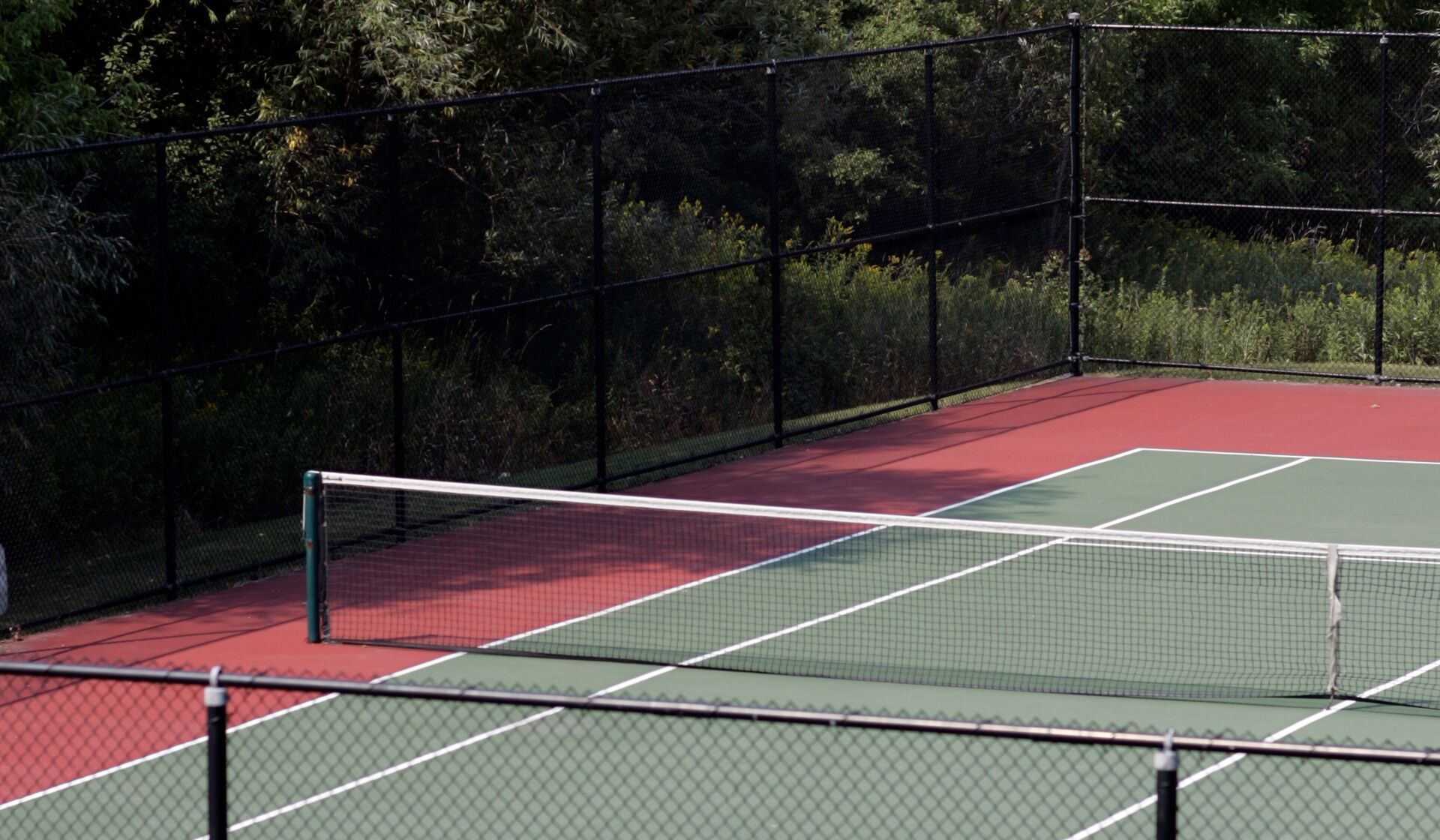 Empty tennis court with net, red and green surface, and trees in the background