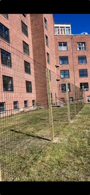 Red brick apartment buildings beside a fenced grassy courtyard under a clear blue sky.